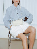 Reco Casa ivory leather compact baguette bag with adjustable strap and key charm, worn by a model sitting.