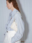 Reco Casa ivory leather baguette bag with adjustable strap and signature key charm, worn crossbody by a woman.