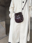 Reco Clam Shell crossbody bag in deep red coral with kiss-lock clasp and natural pleats, worn by a person in a cream coat.