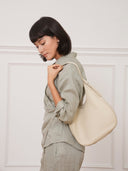 A woman wearing a Reco. Halston white Togo calfskin hobo bag over her shoulder against a neutral studio background.