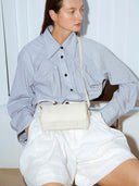 Reco ivory leather compact baguette bag with adjustable strap and signature key charm, worn crossbody by a model.