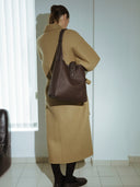 Reco Key Hobo bag in rosewood pebbled leather with white stitching and a signature key closure. Worn by a model in a tan coat.