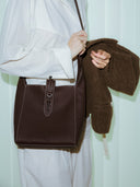 Reco Key Hobo bag in rosewood pebbled leather with white stitching and a key closure. Worn by a woman.