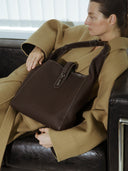 Reco Key Hobo bag in rosewood pebbled leather with white stitching and a signature key closure. A woman wears it on her shoulder.