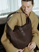 Reco Key Hobo bag in rosewood pebbled leather with white stitching and a signature key closure. Model wears a tan coat.