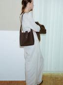 Reco Key Hobo (22) rosewood pebbled leather shoulder bag with key closure and white stitching. Model wears white outfit.
