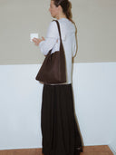 Reco Key Hobo bag in rosewood pebbled leather with a key closure. Model wears a light blue sweater and dark skirt.
