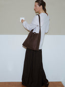 Reco Key Hobo (30) rosewood pebbled leather tote bag with key closure and white stitching. Model wears a cream sweater and dark skirt.