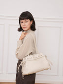 Model wearing a Reco. L'erreur dumpling bag in Fog White pebbled Togo calfskin with a drawstring closure.