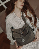 Reco Myway suede crossbody bag in muted olive green with zipper closure and compass pendant. Model wears a plaid shirt.