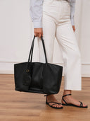 Reco. Ordo midnight black Napa leather dumpling tote bag with pleated front, held by a model in white trousers.