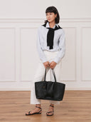 Model holding a black Reco. Ordo Napa leather dumpling tote bag with a pleated front in a minimalist studio setting.