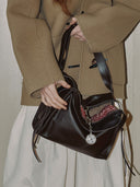 Reco. Rosewood leather shoulder bag with a compass charm and a flying-tail zipper, worn by a person in a tan coat.