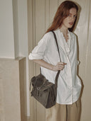 Reco Wander bag in algae suede with a compass charm and flying-tail zipper, worn by a model.