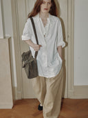 Reco Wander bag in algae suede with a compass charm and flying-tail zipper, worn by a model with red hair.