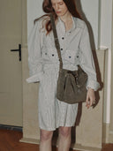 Reco Wander bag in algae suede with a compass charm and flying-tail zipper, worn by a model in a plaid dress.