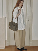 Reco Wander bag in algae green suede with a compass charm and flying-tail zipper, worn by a model with long red hair.
