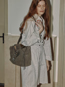 Reco Wander bag in algae suede with a compass charm and flying-tail zipper, worn by a model in a plaid dress.