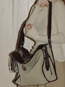 Reco Wander bag in beige canvas with dark brown leather trim and a compass charm. Features a relaxed silhouette and flying-tail zipper.