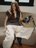 Reco Wander bag in ebony sand suede with black leather trim and a compass charm. Model wears a brown knit vest and cream pants.