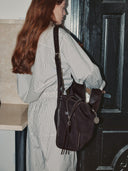 Reco Wander bag in espresso brown textured material with a compass charm and flying-tail zipper, worn by a woman.