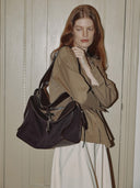 Reco Wander (L) espresso brown textured shoulder bag with leather trim and compass charm. Model wears a tan jacket.