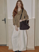 Reco Wander bag in espresso brown suede with a compass charm and flying-tail zipper, worn by a model with red hair.