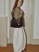Reco Wander bag in espresso brown suede with a compass charm and flying-tail zipper, worn by a model.