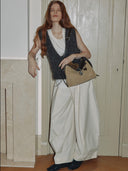 Reco. Wander bag in tan suede with dark brown leather trim and compass charm. Model wears a grey vest and cream pants.