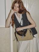 Reco. Wander bag in tan suede with dark brown leather trim and compass charm. Model wears a grey vest and white top.