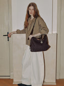Reco Wander bag in espresso brown suede with a compass charm and flying-tail zipper, worn by a model.