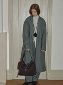 Reco Wander (L) espresso brown suede slouchy bag with compass charm and flying-tail zipper, worn by a model in a grey coat.