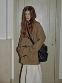 Reco Wander bag in rosewood leather with a compass charm, worn by a model in a tan duffle coat.