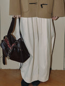 Reco Wander bag in rosewood leather with compass charm and flying-tail zipper, held by a model wearing a tan coat.