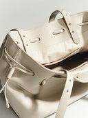 Reco. L'erreur dumpling bag in Fog White pebbled Togo calfskin with drawstring closure and gold hardware details.